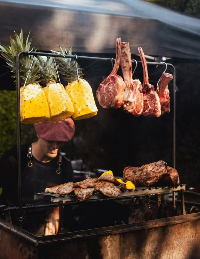 Parrilla en vivo de El Ombú con piñas, costillares y carne sobre las brasas en un evento outdoor